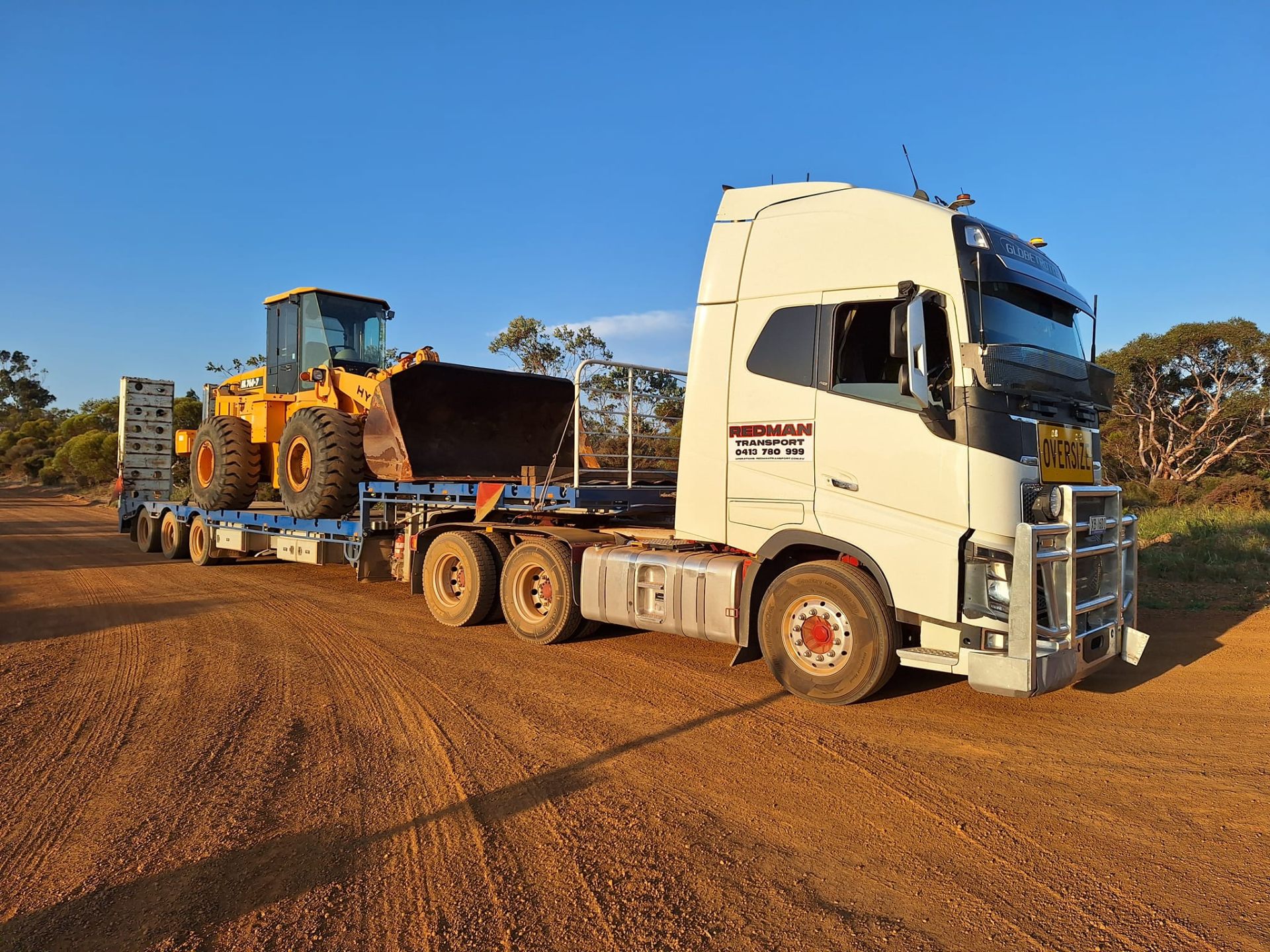 Redman Transport Volvo prime mover hauling a wheel loader on a WA outback road